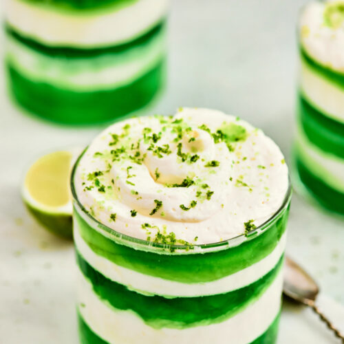 A glass filled with alternating layers of green gelatin and white cream, topped with whipped cream and green zest—these St. Patrick’s Day Green Jello Parfaits are a festive treat perfect for celebrating.