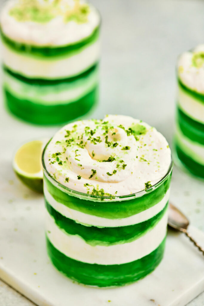 A glass filled with alternating layers of green gelatin and white cream, topped with whipped cream and green zest—these St. Patrick’s Day Green Jello Parfaits are a festive treat perfect for celebrating.