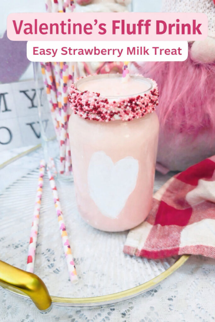 A mason jar filled with pink Strawberry Milk, topped with pink and white sprinkles, and a heart shape on the front, sits beside decorative straws and a checkered napkin—a perfect Valentine Treat.